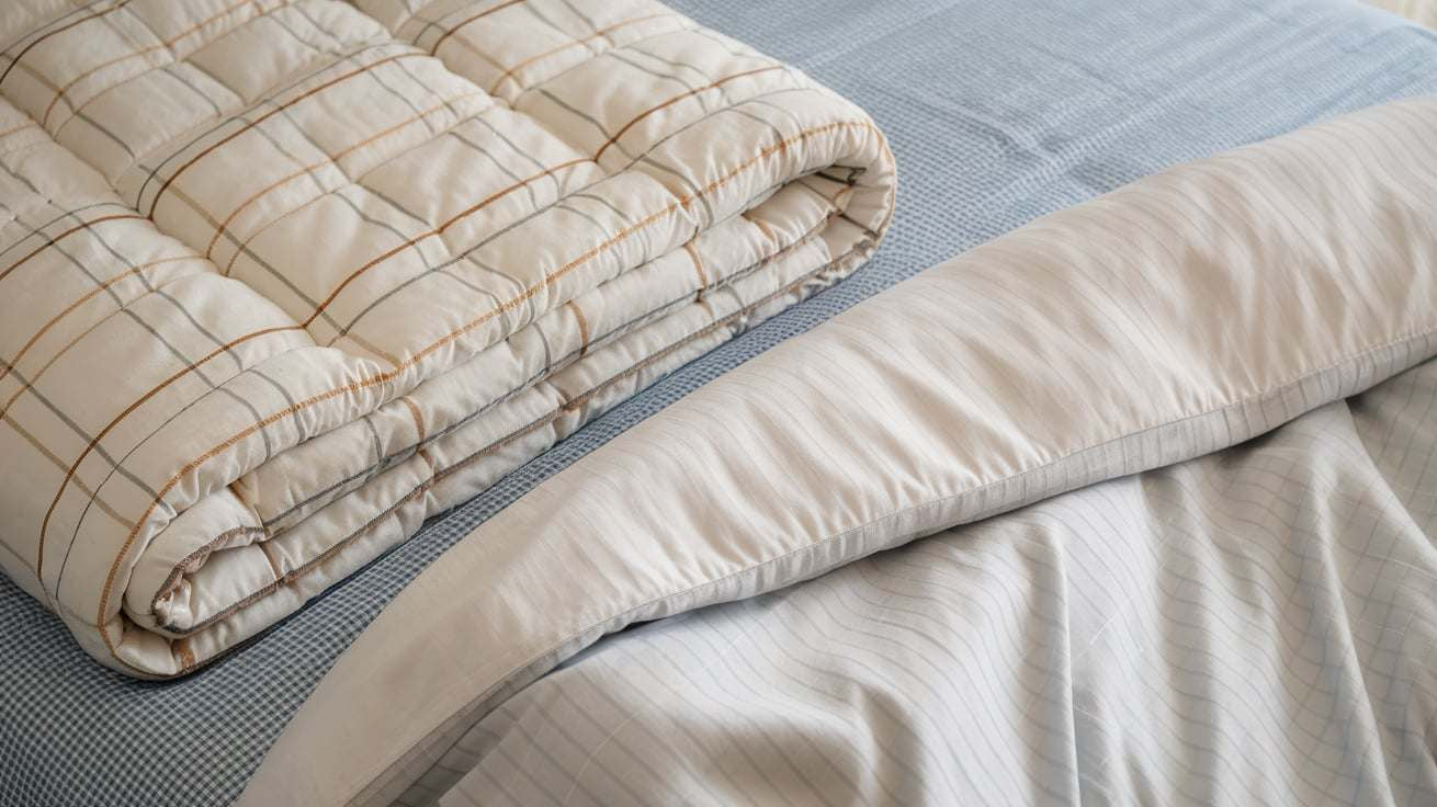 a comforter and a duvet. The comforter is a thick, fluffy white blanket with a plaid pattern and is folded neatly on a bed